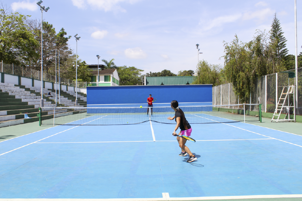 El Departamento de Deportes UIS invita a que se conozca sus Canchas de Tenis. Plano general del escenario deportivo donde aparecen dos estudiantes jugando tenis.