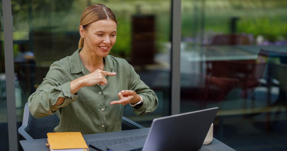 fotografía de una mujer frente a un computador realizando lengua de señas